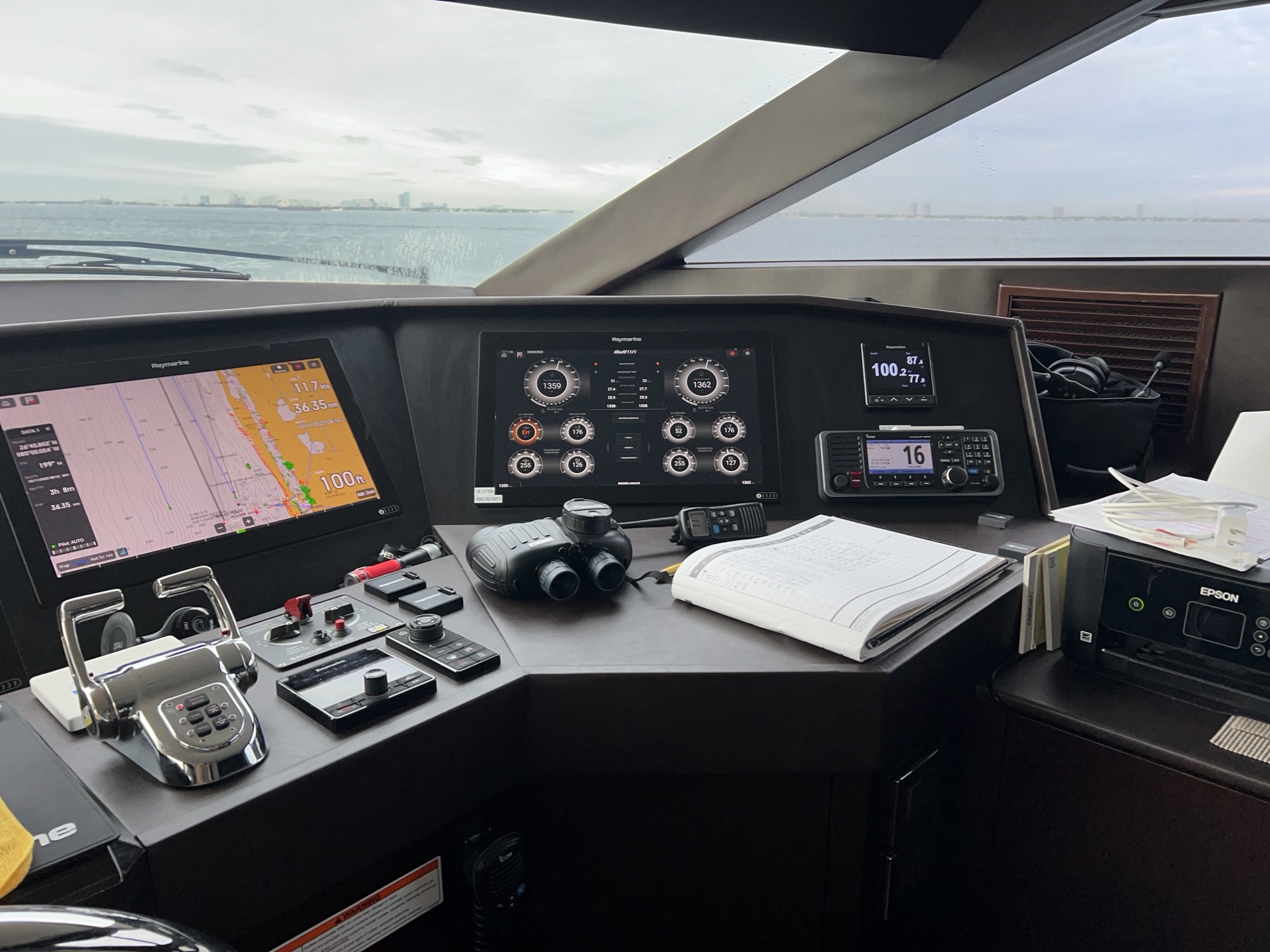 Flybridge helm station with gauges and chartplotter, city skyline on the horizon